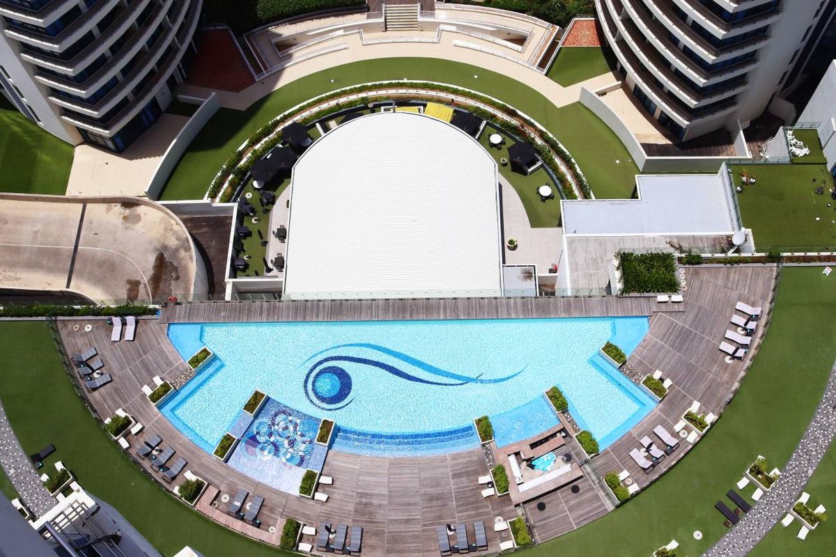 Aerial view of a modern apartment complex featuring a large swimming pool, landscaped garden areas, and timber decking.