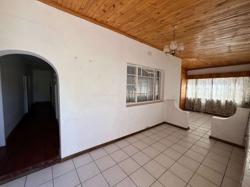 An empty living room featuring a timber tongue and groove ceiling, ceramic tiled flooring, and a distinctive arched entryway.