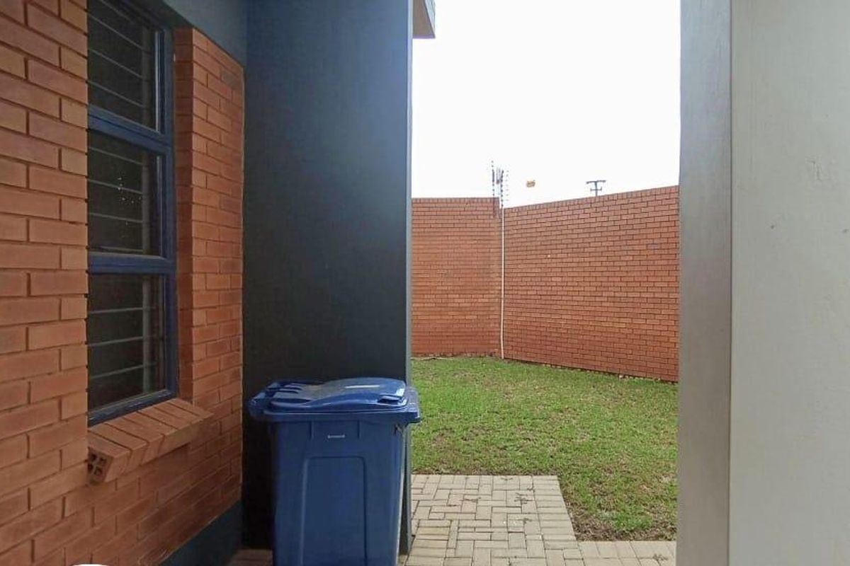 A view of the rear garden area featuring a paved walkway, brick boundary walls, and a covered patio section.