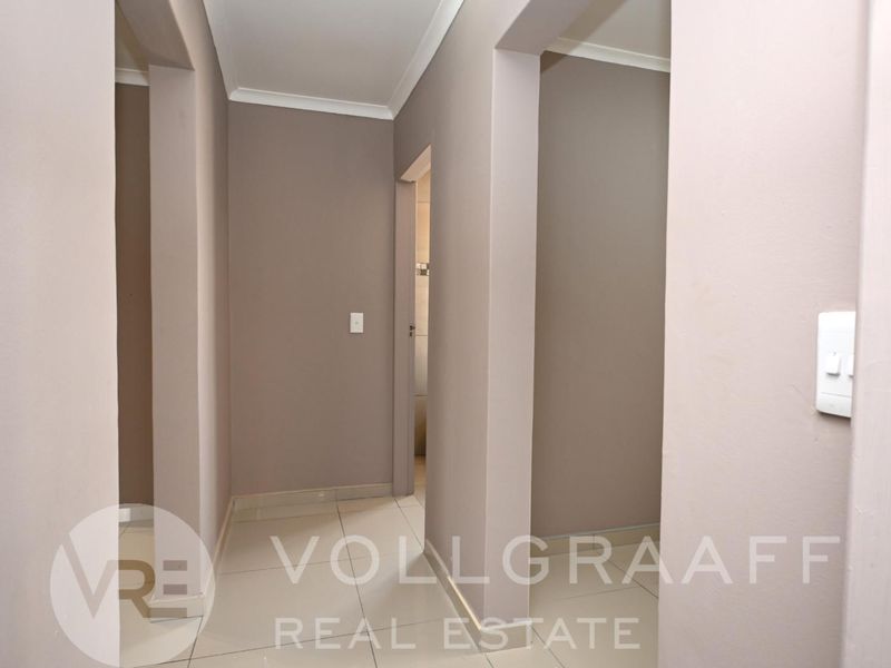 A clean, neutral-toned hallway featuring tiled flooring and coved cornicing, providing access to multiple rooms within the property.