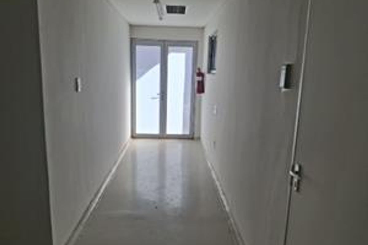 A clean, empty office hallway featuring white walls, smooth flooring, and double glass doors providing natural light access.