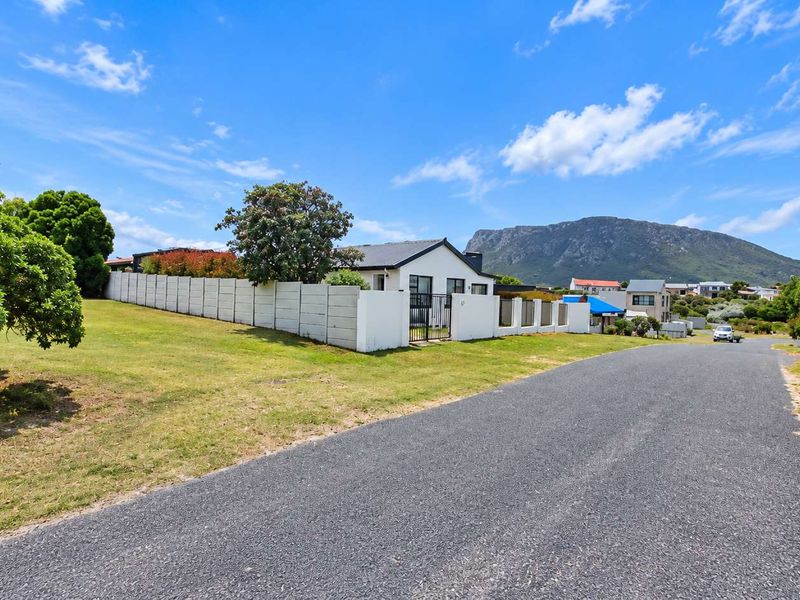 Street view of a residential property featuring a precast concrete boundary wall, metal gate, and surrounding landscaped grounds with mountain views.