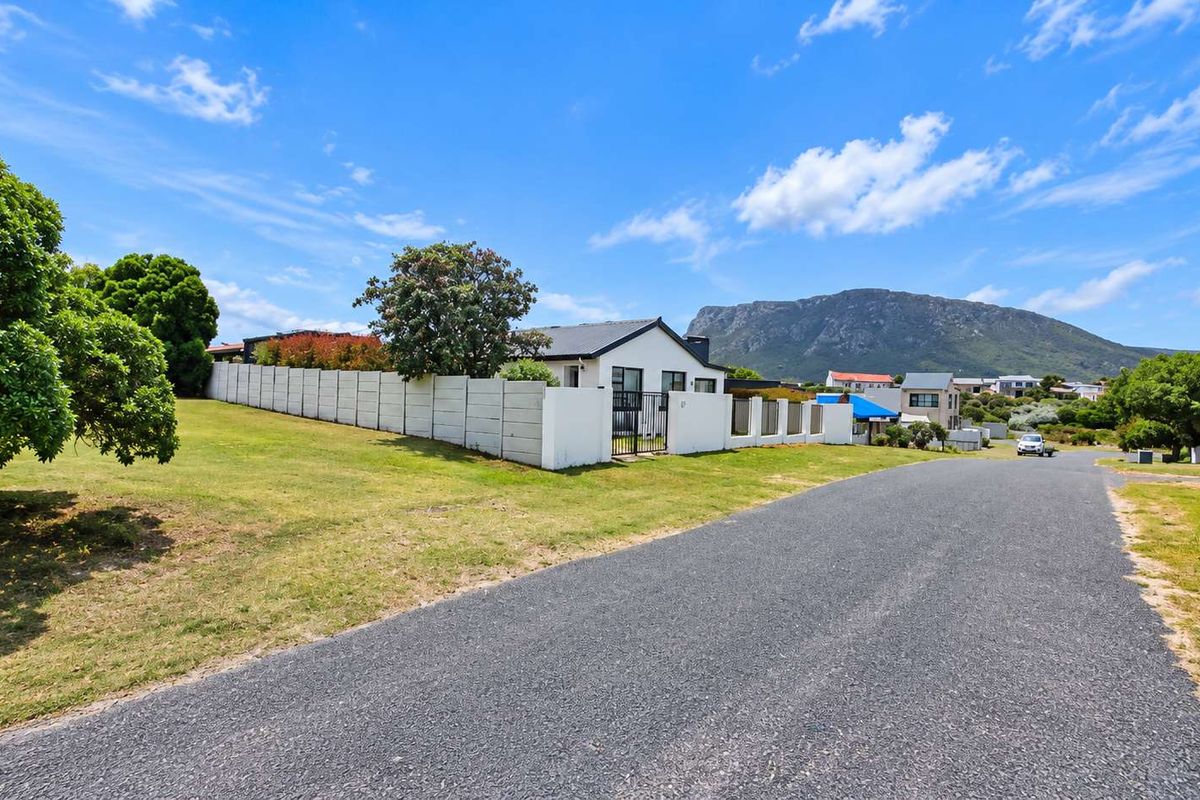 Street view of a residential property featuring a precast concrete boundary wall, metal gate, and surrounding landscaped grounds with mountain views.
