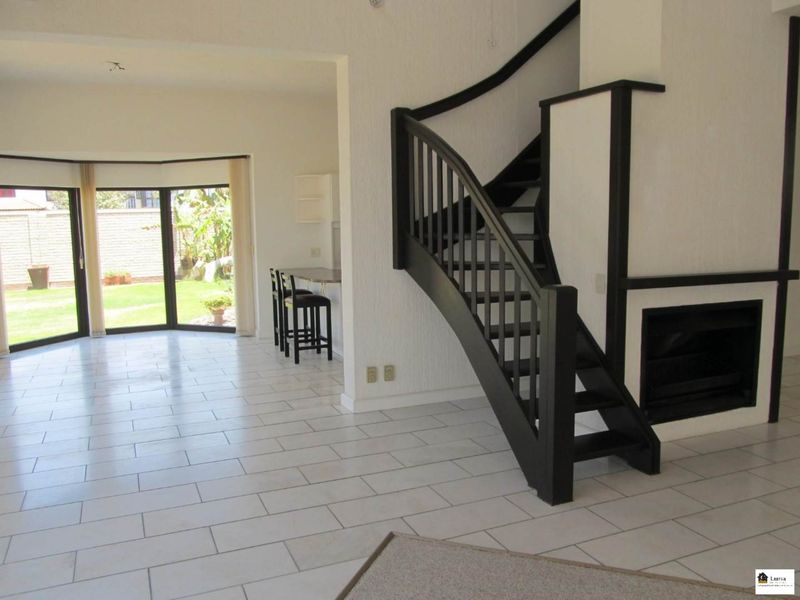 Spacious open-plan living area featuring a striking black staircase, built-in fireplace, tiled flooring, and large sliding doors leading to the garden.