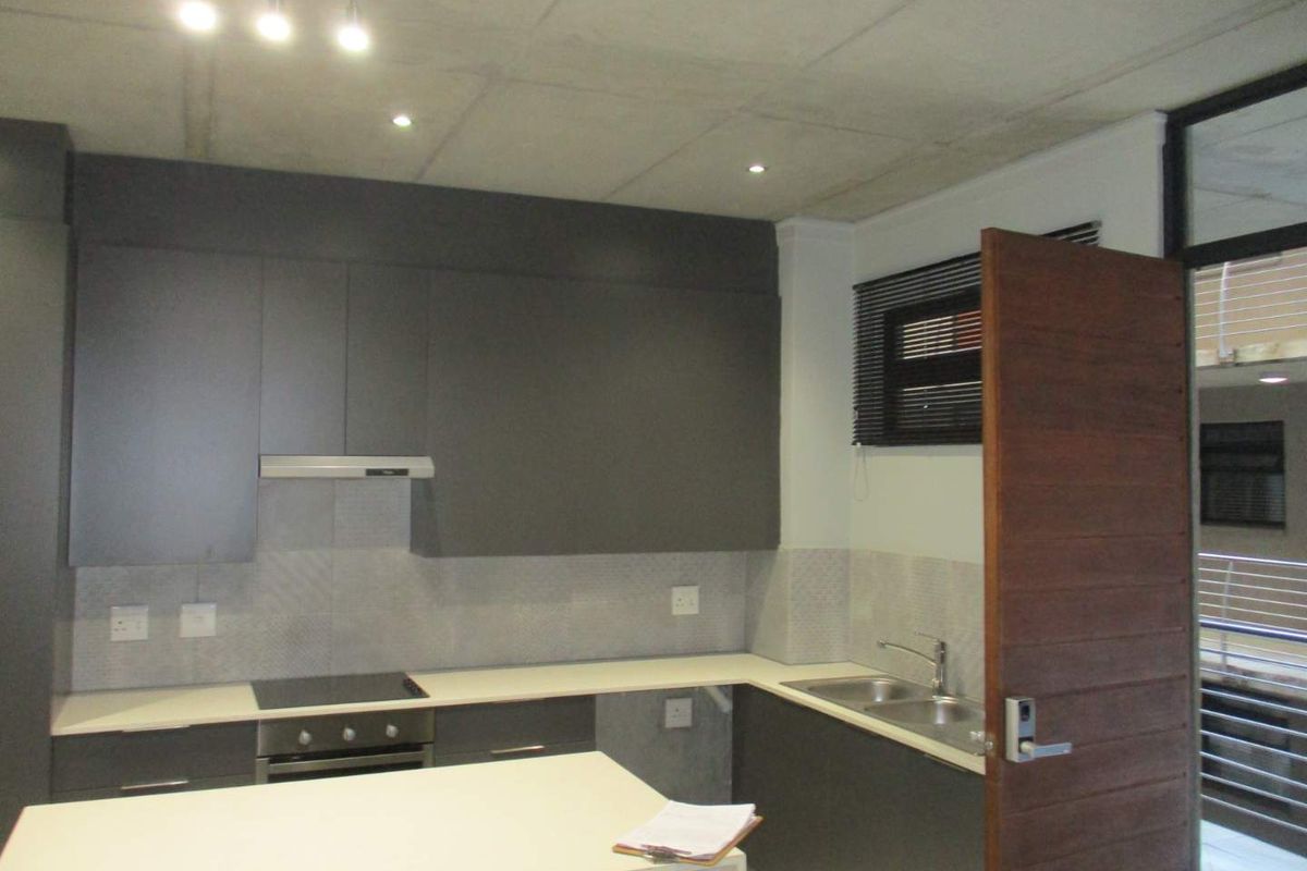Modern kitchen featuring dark grey cabinetry, light countertops, integrated oven and hob, stainless steel double sink, and exposed concrete ceiling finish.
