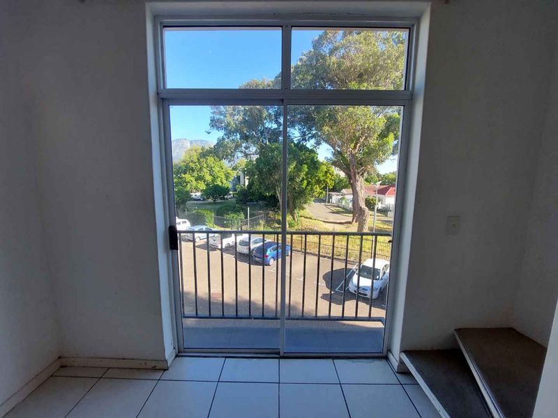 A bright, empty balcony area featuring tiled flooring, a sliding glass door, and a metal balustrade with views of the surrounding neighborhood.