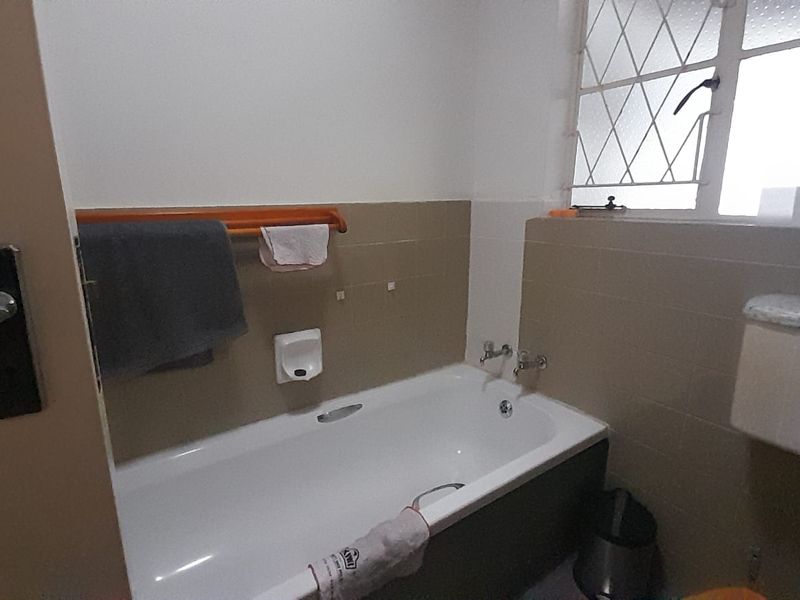 A functional bathroom featuring a standard bathtub with tiled splashback and a window with security bars.