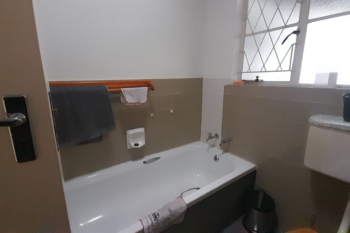 A functional bathroom featuring a standard bathtub with tiled splashback and a window with security bars.