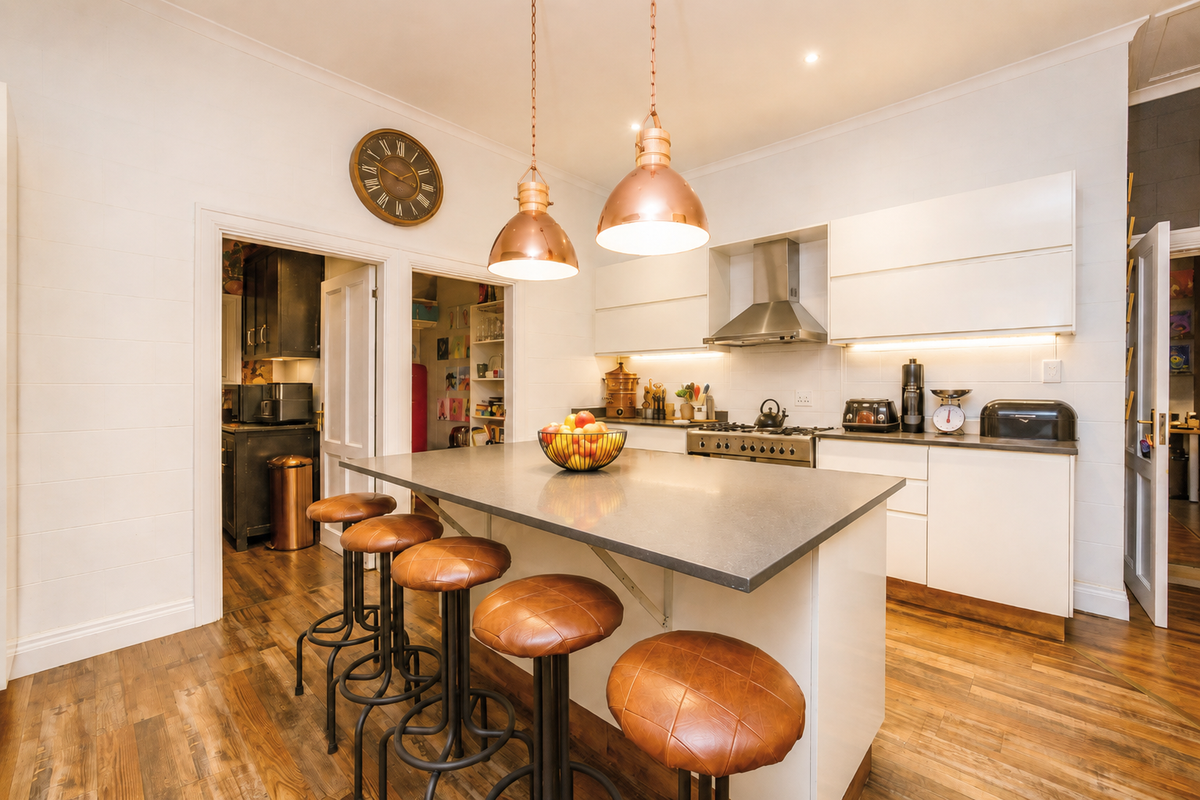 Modern kitchen featuring a central island with stone countertops, built-in gas cooktop, stainless steel extractor, and warm pendant lighting, complemented by hardwood flooring.