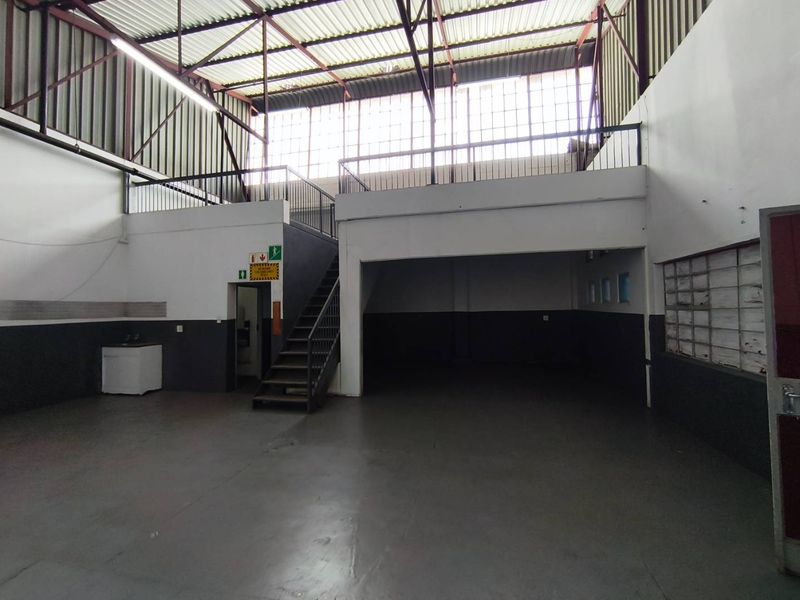 Spacious industrial utility area featuring a mezzanine level, steel staircase, exposed roof trusses, and durable concrete flooring, suitable for warehouse or workshop use.