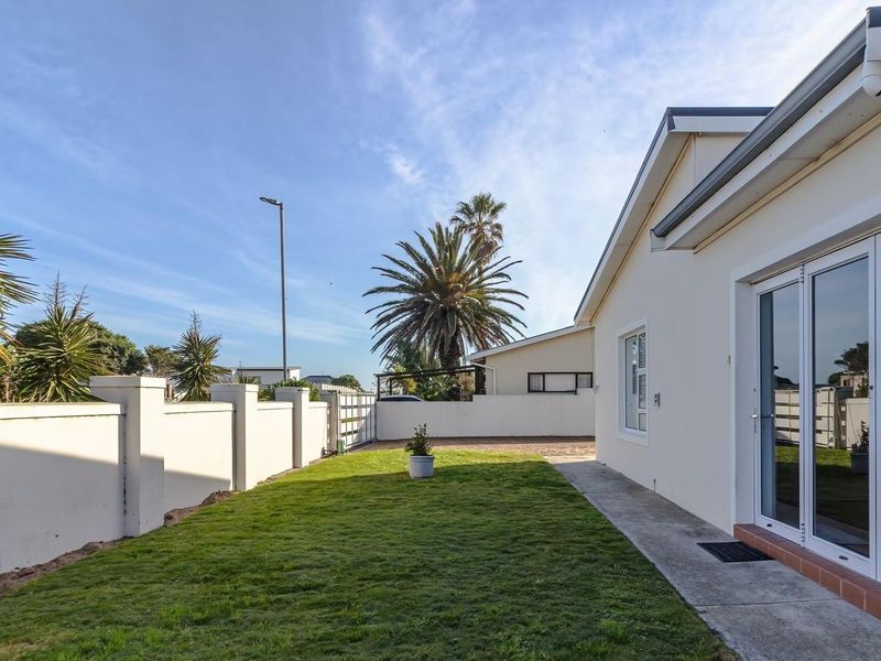 A well-maintained rear garden area featuring a neat lawn, concrete pathway, and sliding glass door access to the main dwelling.