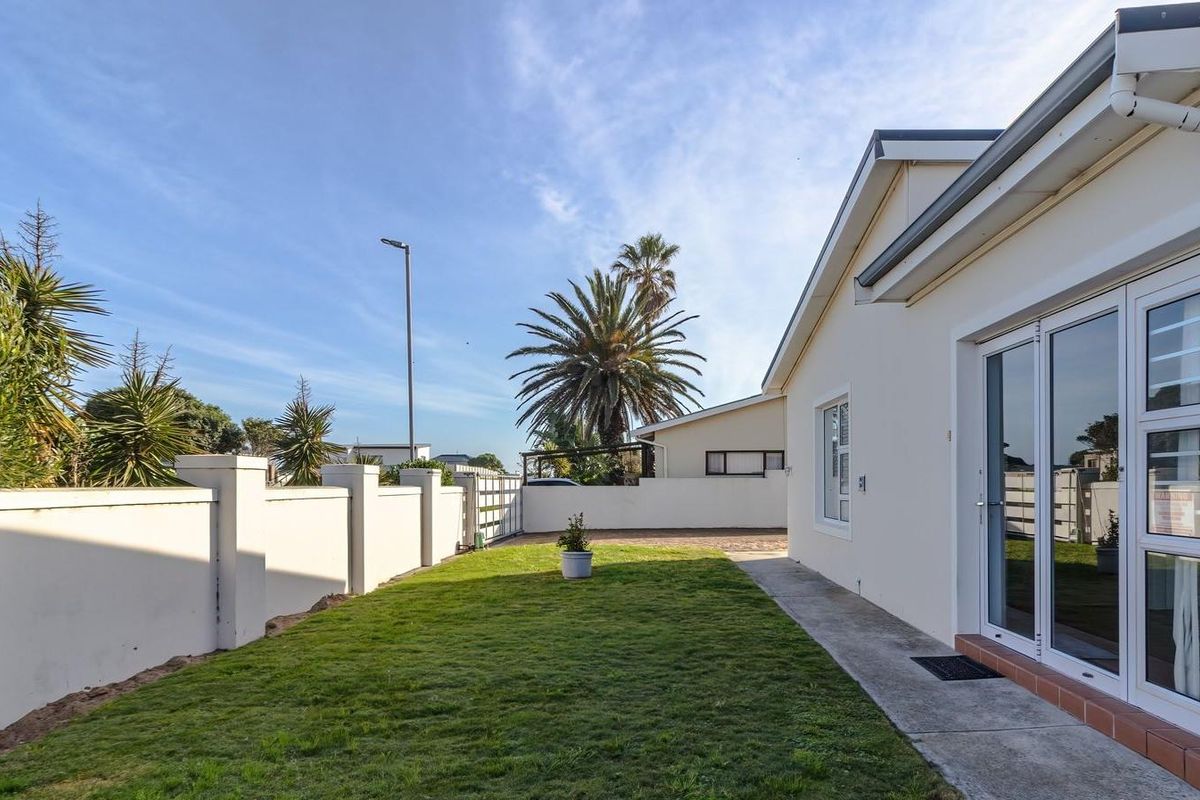 A well-maintained rear garden area featuring a neat lawn, concrete pathway, and sliding glass door access to the main dwelling.