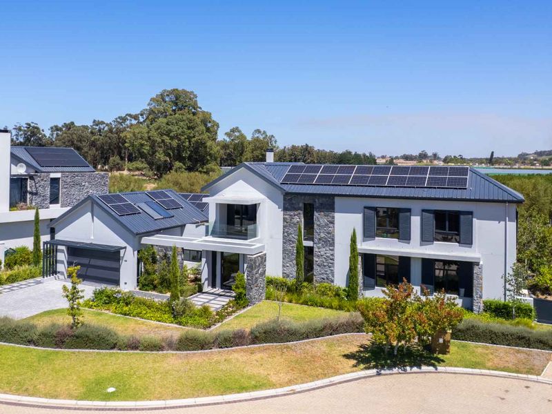 Modern double-story residence featuring stone cladding, solar panels, a paved driveway, and a well-maintained landscaped garden.
