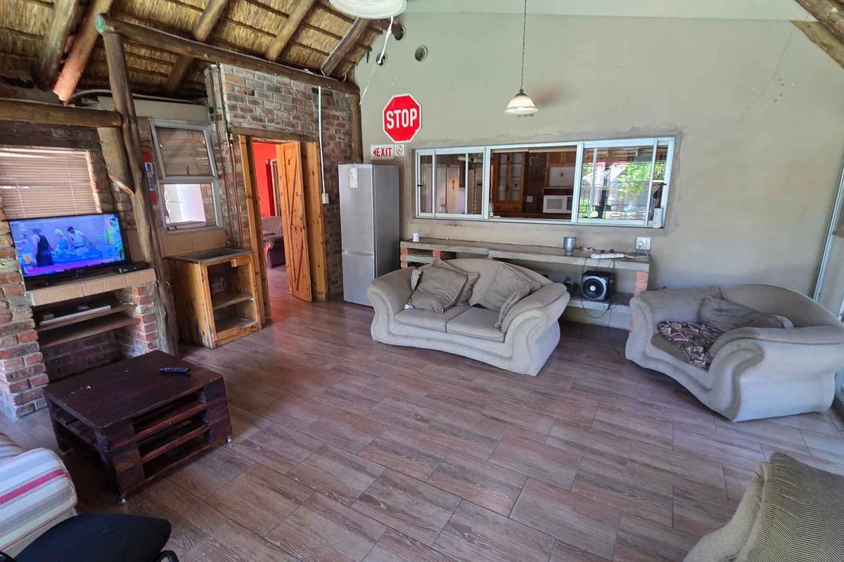 Spacious living area featuring a rustic thatched roof, exposed brick accents, tiled flooring, and a large serving window connecting to the kitchen area.