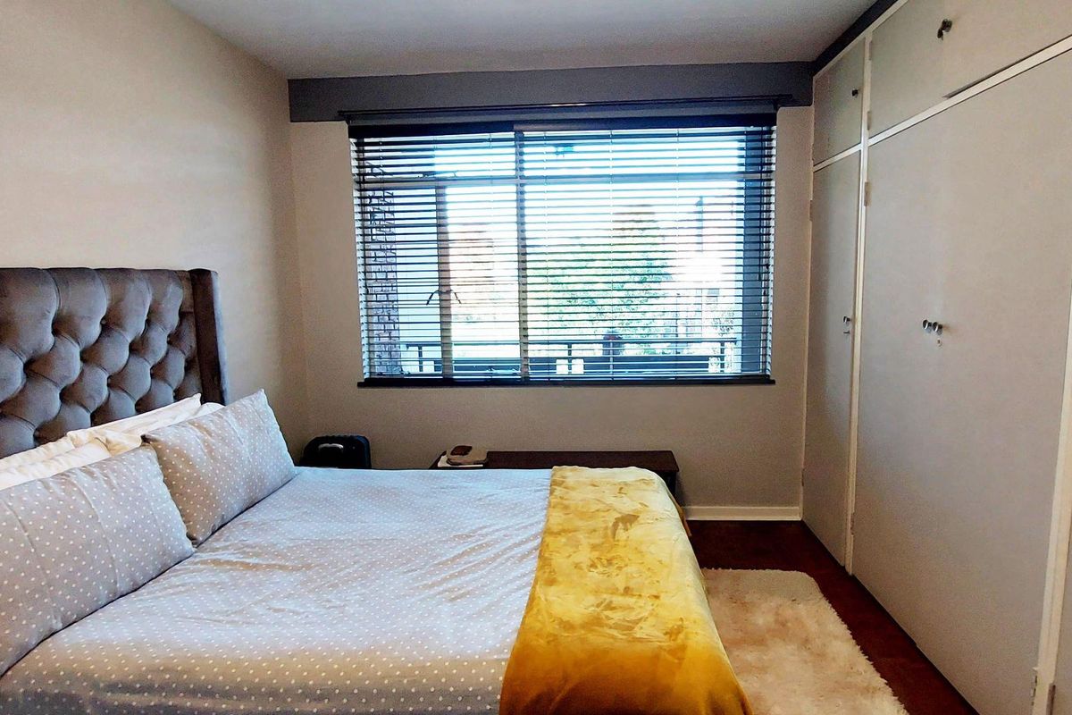 A well-lit bedroom featuring hardwood flooring, built-in cupboards for storage, and venetian blinds on the window.