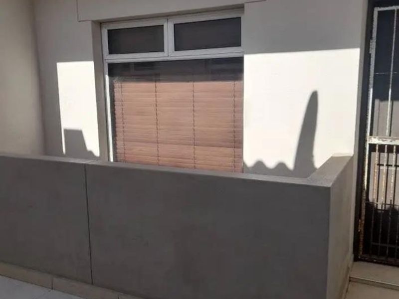 A clean, tiled balcony area featuring a solid concrete balustrade and a secure entrance door, providing a private outdoor space.