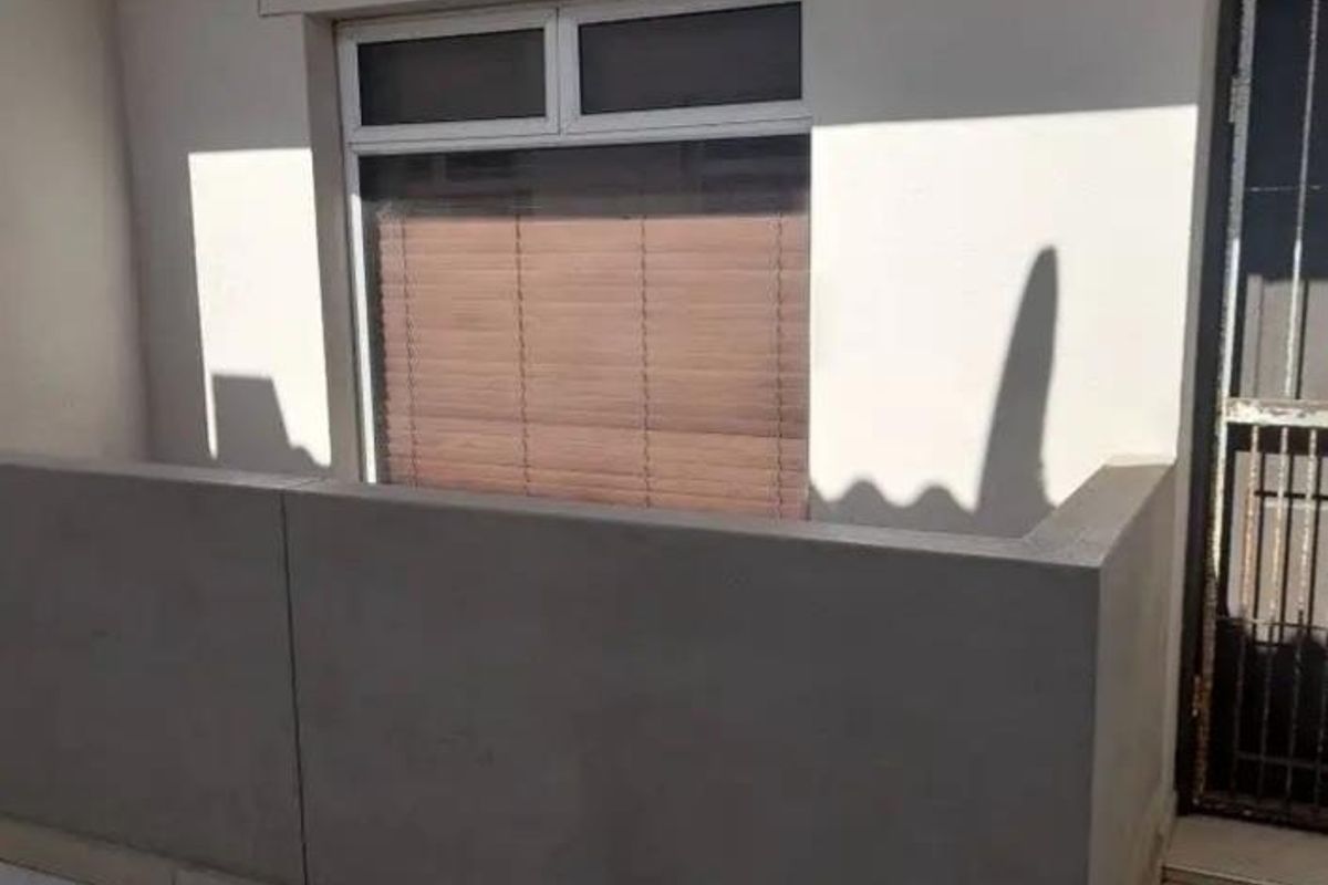 A clean, tiled balcony area featuring a solid concrete balustrade and a secure entrance door, providing a private outdoor space.