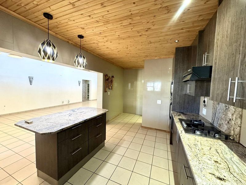 Modern kitchen featuring granite countertops, a central island, gas hob, extractor fan, and built-in oven, seamlessly flowing into an open-plan living area.