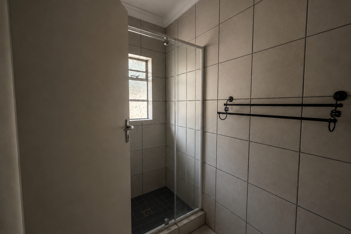 A functional bathroom featuring a tiled shower enclosure with a glass door, neutral wall tiling, and a wall-mounted towel rail.
