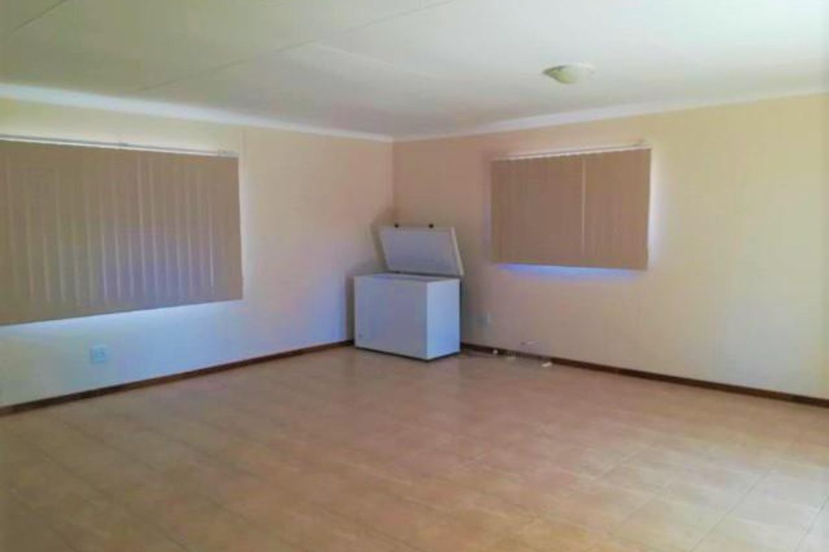 A spacious, empty living area featuring neutral tiled flooring, vertical window blinds, and recessed ceiling lighting.
