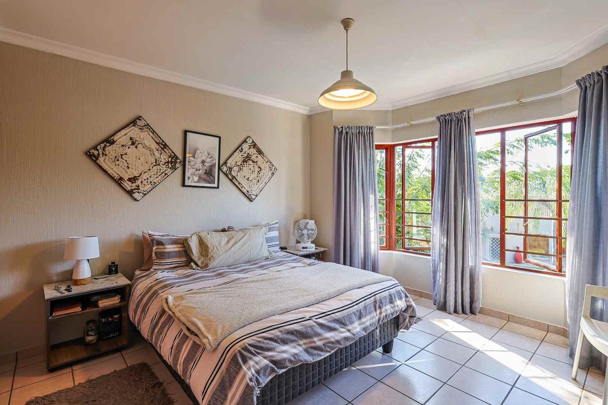 A well-lit bedroom featuring tiled flooring, a bay window with natural light, and coved ceiling details.