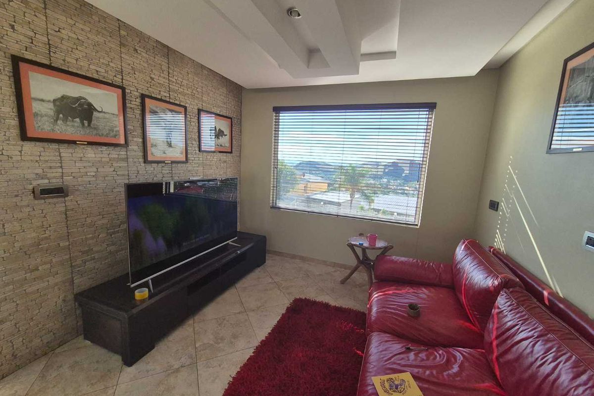 A comfortable living room featuring a textured stone feature wall, recessed ceiling lighting, and large windows offering natural light and views.