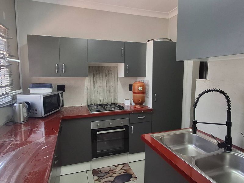 A functional kitchen featuring dark grey cabinetry, red countertops, a gas hob, built-in oven, and a double basin sink with a modern gooseneck faucet.
