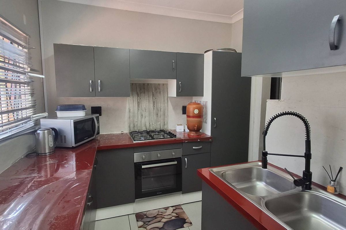 A functional kitchen featuring dark grey cabinetry, red countertops, a gas hob, built-in oven, and a double basin sink with a modern gooseneck faucet.