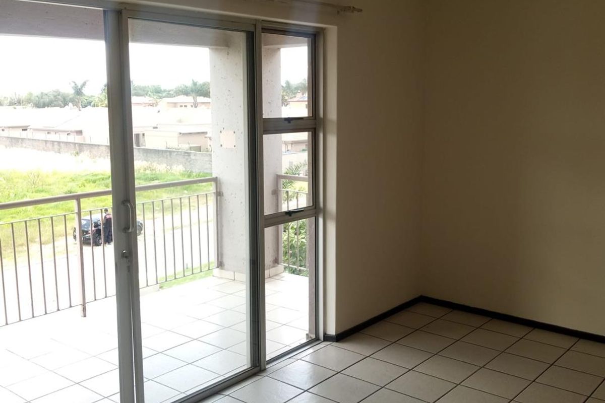 An empty living area featuring tiled flooring and large sliding glass doors that open onto a private balcony with outdoor views.
