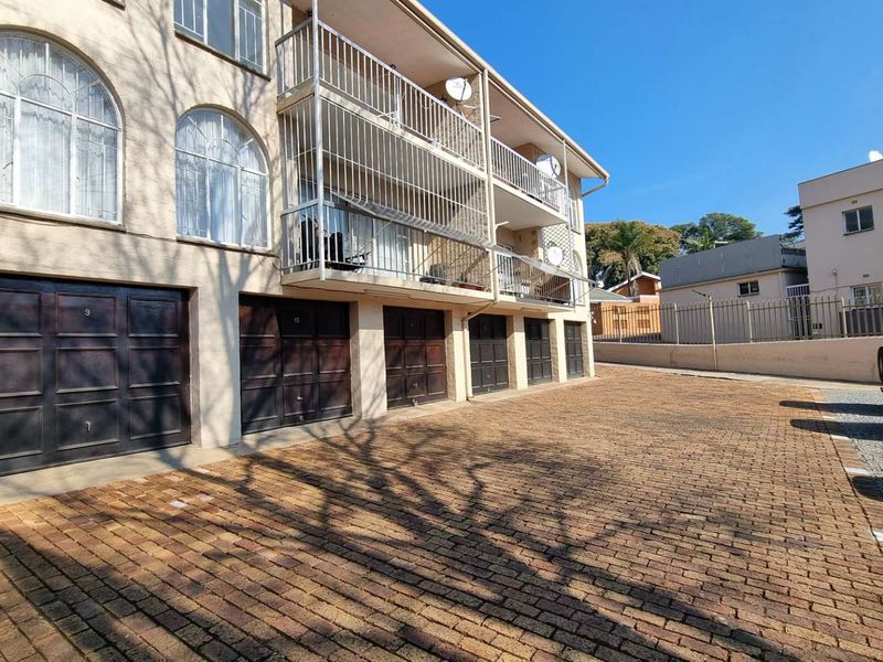 Exterior view of an apartment complex featuring a brick-paved driveway, multiple ground-level garages, and upper-level balconies with metal railings.