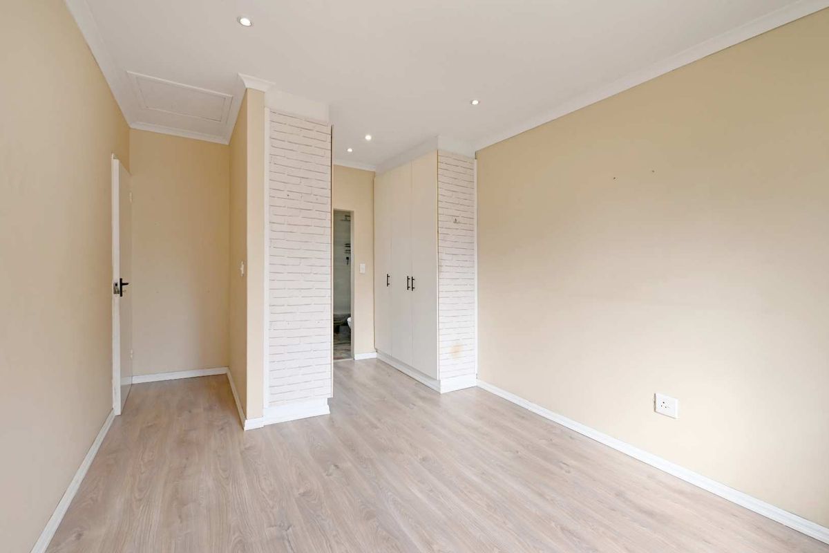 A bright, empty bedroom featuring light laminate flooring, built-in cupboards, and decorative brick-effect columns, offering a clean canvas for personalization.