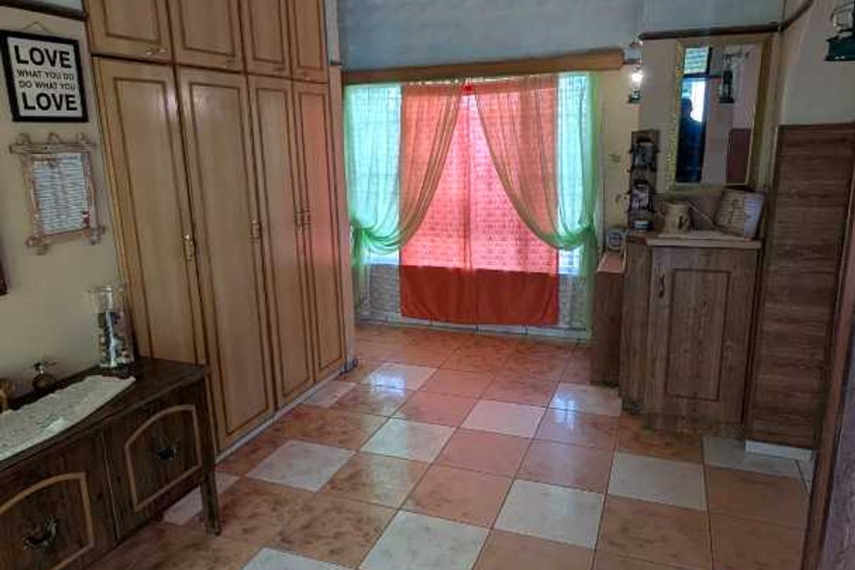 A bedroom featuring built-in wooden wardrobes, tiled flooring, and a vanity area with natural light from the window.
