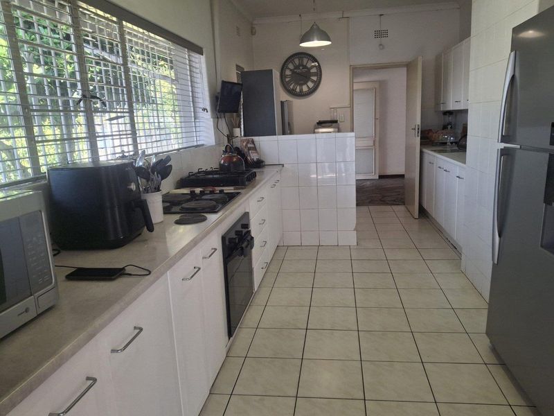 A functional kitchen featuring white cabinetry, tiled flooring, built-in oven and hob, and ample counter space with natural light from large windows.