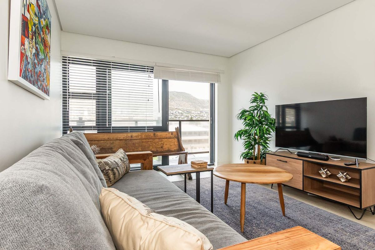 A bright and modern living room featuring large windows with integrated blinds, providing natural light and access to an outdoor balcony area.