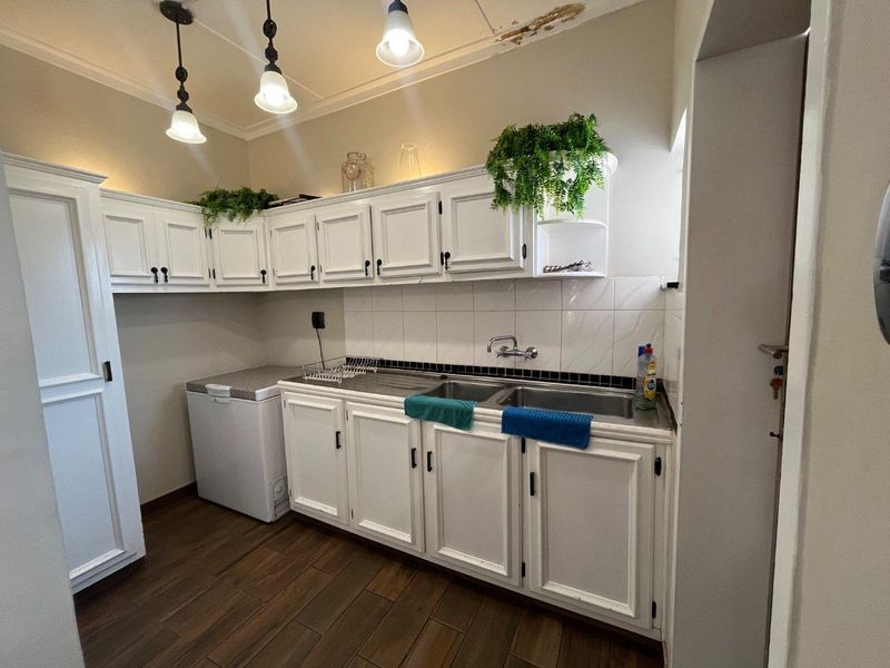 A functional scullery area featuring white built-in cabinetry, a double basin sink, and tiled splashback, with visible ceiling water damage requiring repair.