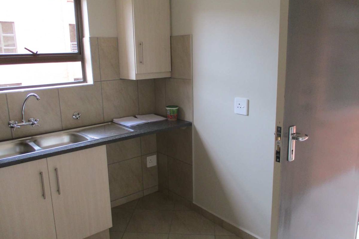 A compact, functional kitchen area featuring light-toned cabinetry, granite countertops, a stainless steel double sink, and neutral tiled finishes.