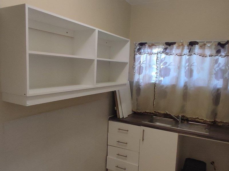 A functional laundry area featuring built-in cabinetry, a stainless steel sink, and wall-mounted shelving, providing practical utility space.