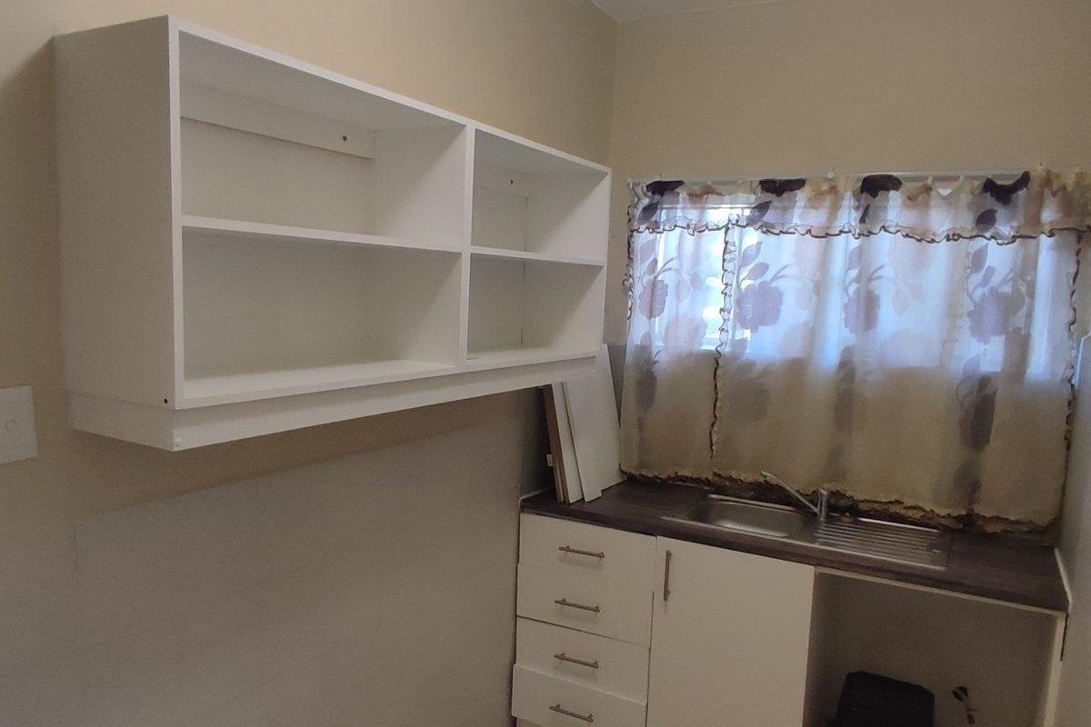 A functional laundry area featuring built-in cabinetry, a stainless steel sink, and wall-mounted shelving, providing practical utility space.
