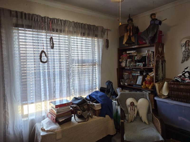 A bedroom featuring a large window with venetian blinds and curtain rod, showing signs of wear on the ceiling.