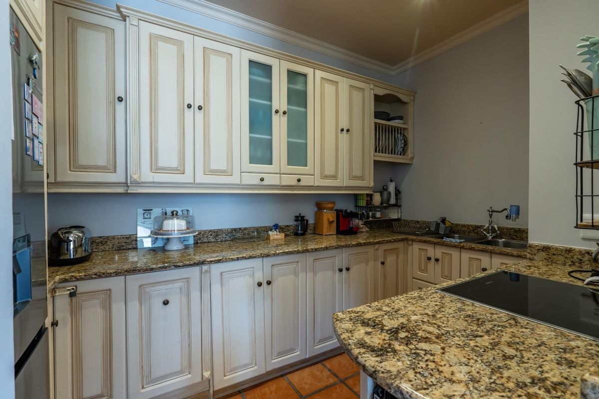 A functional kitchen featuring cream-toned cabinetry, granite countertops, and terracotta floor tiles, offering ample storage and workspace.