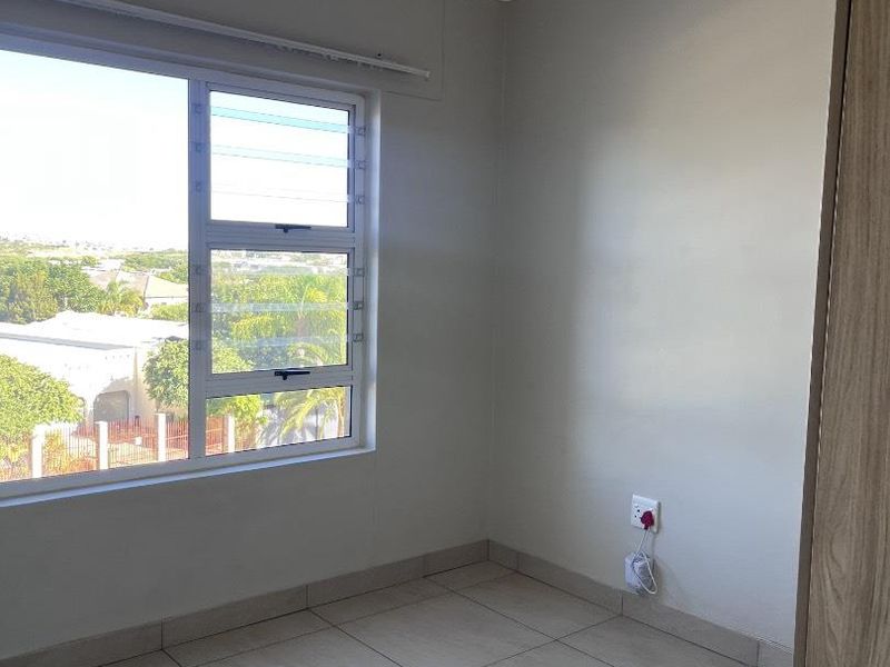 A bright, empty bedroom featuring neutral tiled flooring, built-in cupboards, and a large window with views of the surrounding area.