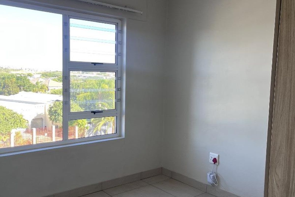 A bright, empty bedroom featuring neutral tiled flooring, built-in cupboards, and a large window with views of the surrounding area.