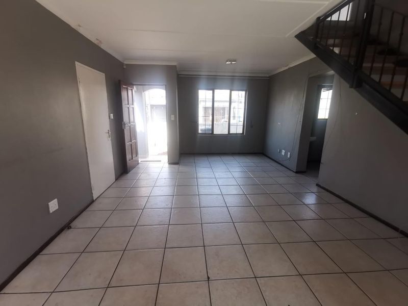 An empty, open-plan living area featuring tiled flooring, a staircase, and neutral grey walls, offering a blank canvas for interior design.
