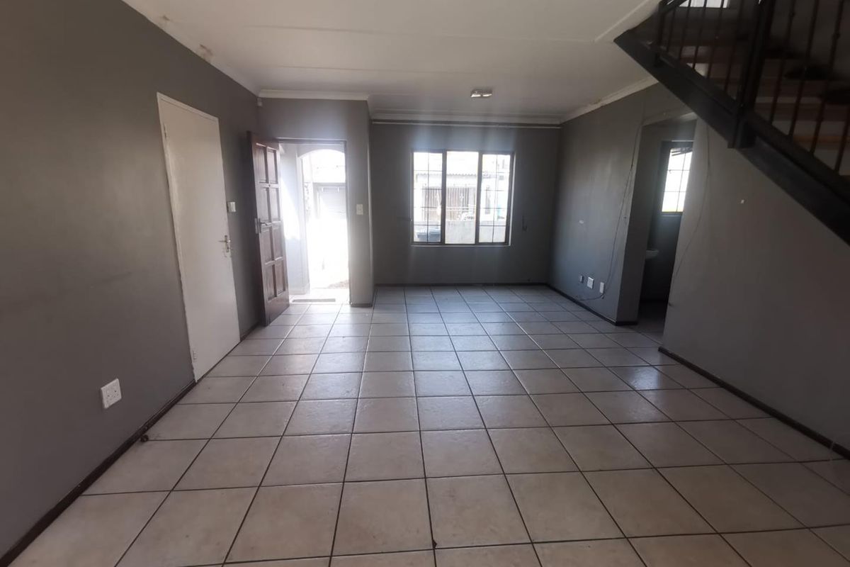 An empty, open-plan living area featuring tiled flooring, a staircase, and neutral grey walls, offering a blank canvas for interior design.
