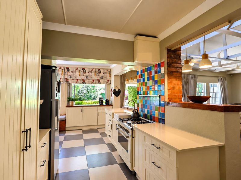 A charming kitchen featuring cream cabinetry, stone countertops, a colorful tiled splashback, and a gas stove, seamlessly connected to the adjacent living area.