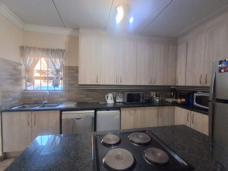 Functional kitchen featuring light wood-finish cabinetry, dark granite countertops, a built-in electric hob, and a tiled backsplash with security bars on the window.