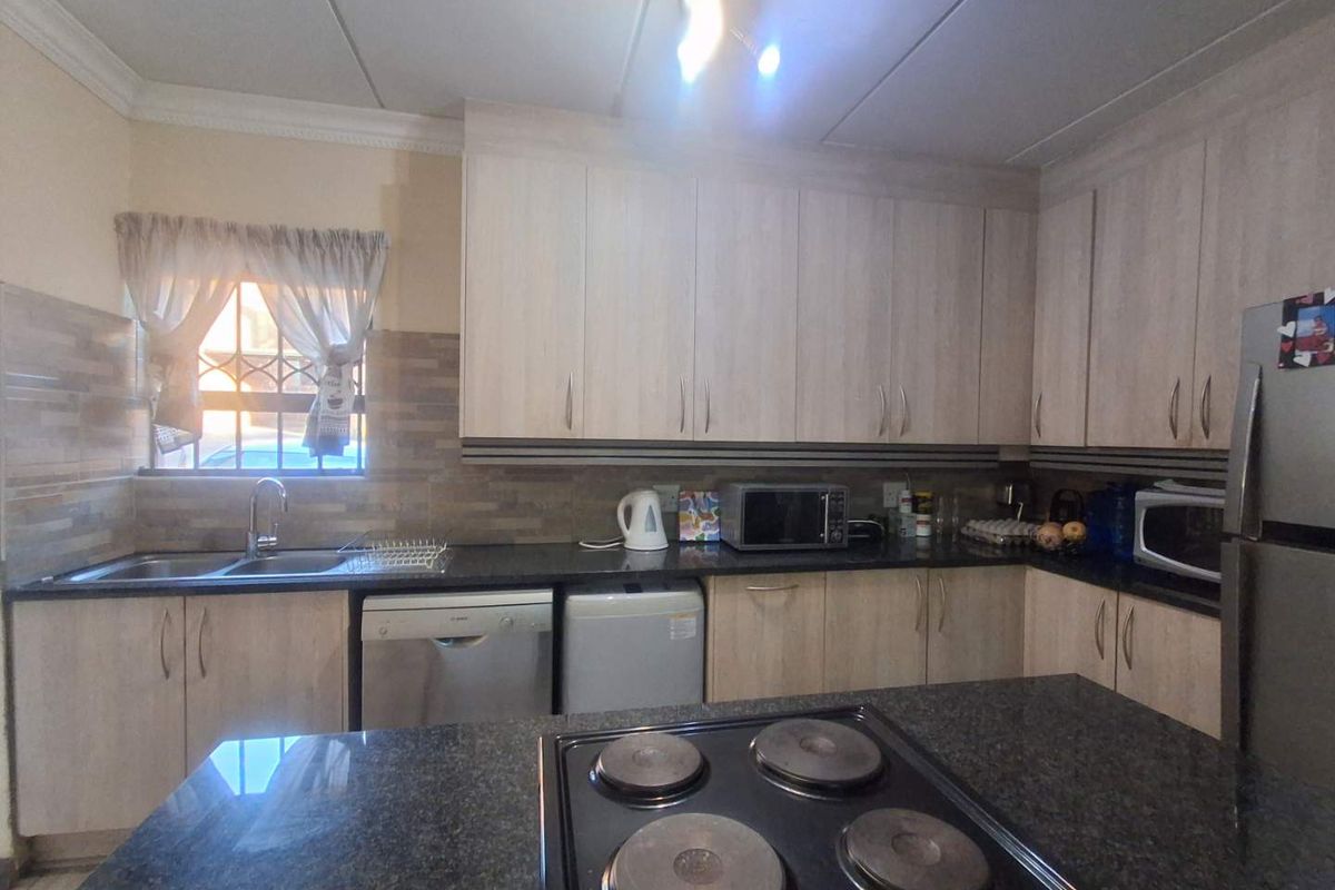 Functional kitchen featuring light wood-finish cabinetry, dark granite countertops, a built-in electric hob, and a tiled backsplash with security bars on the window.