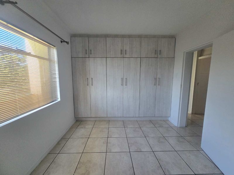 A bright, empty bedroom featuring neutral tiled flooring and extensive built-in wooden cupboards with modern hardware.