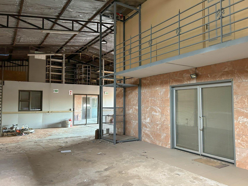 Spacious industrial utility area featuring a mezzanine level, freight lift, and sliding glass doors, offering versatile potential for commercial or workshop use.