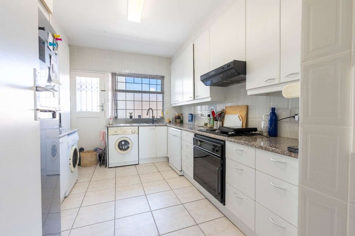 Functional kitchen featuring white cabinetry, granite countertops, built-in oven, hob, extractor fan, and integrated laundry plumbing connections.